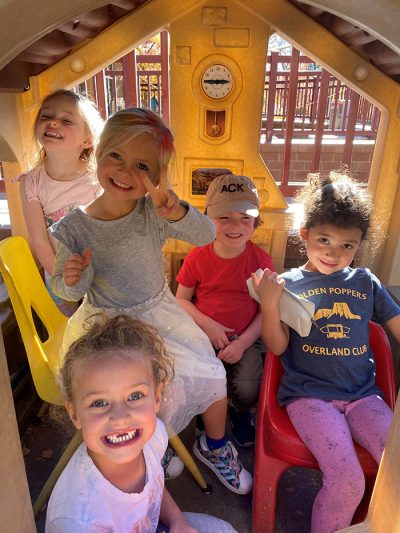 Five girls grin together in a playhouse